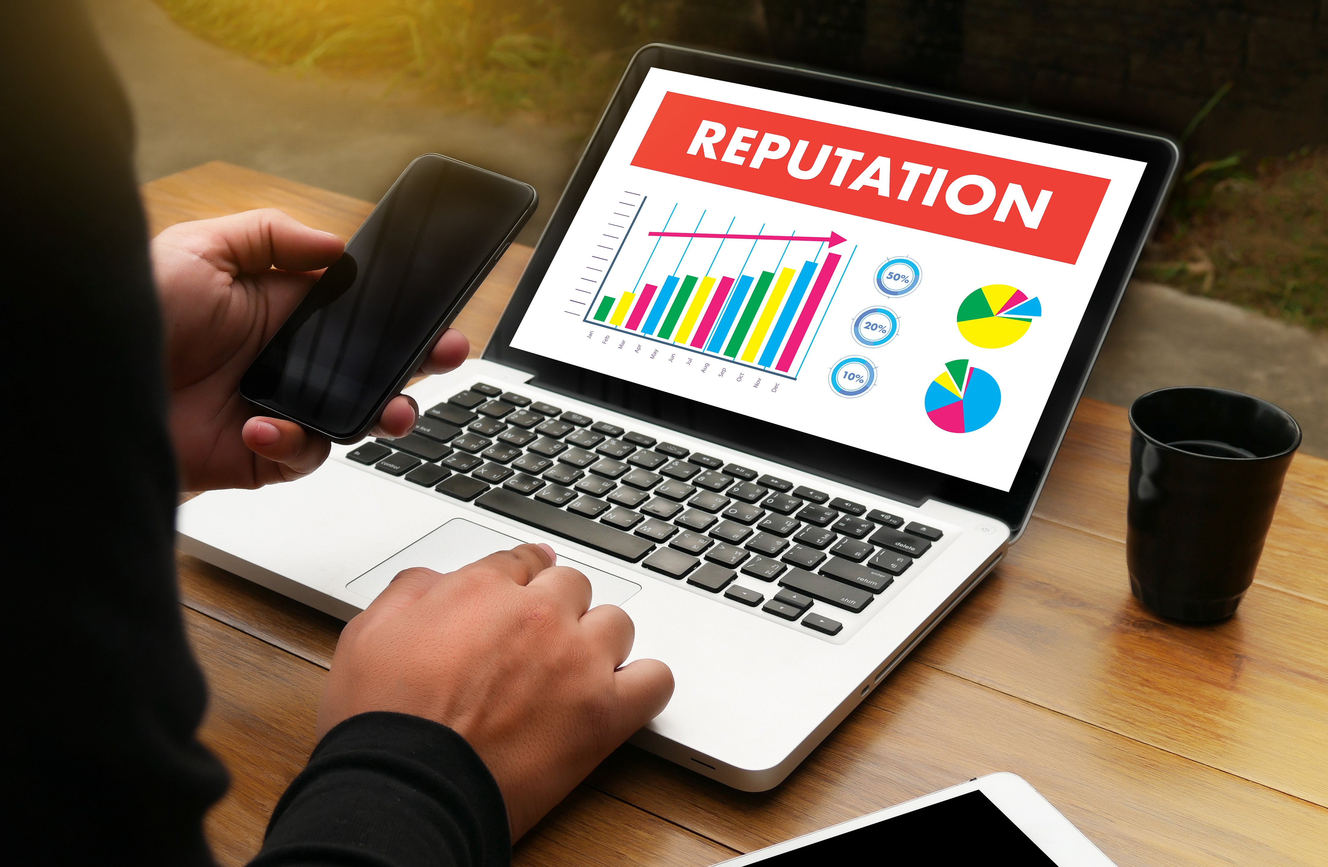 person using phone at laptop with chart of repuation increasing
